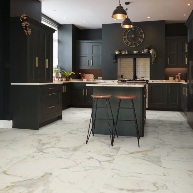 Kitchen with black cabinetry, white counters, and white marble-look tiles, with island with two barstools under pendant lights and wall clock