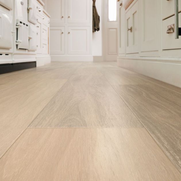 Close up floor-level shot of brown woodgrain LVP floor in kitchen, with white cabinetry, oven door, and entry door in background