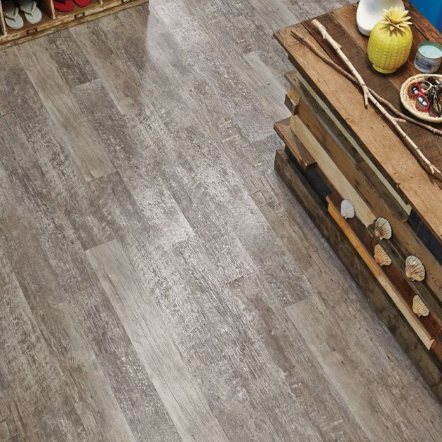 Retail space with aged gray woodgrain flooring, weathered counter topped with sunglasses and pineapple, and cubby shelf filled with flipflops and sneakers