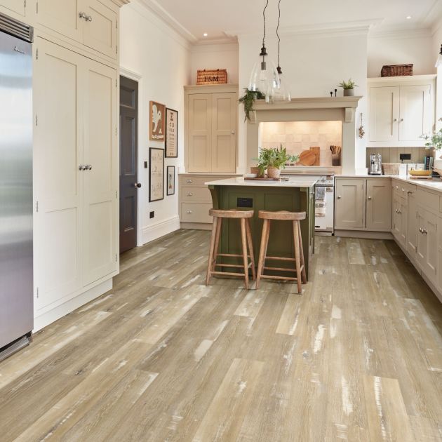 Kitchen with taupe cabinetry, high shade variance taupe woodgrain floor, olive island with stools under pendant lights, with various farmhouse decor