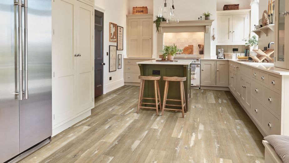 Kitchen with taupe cabinetry, high shade variance taupe woodgrain floor, olive island with stools under pendant lights, with various farmhouse decor