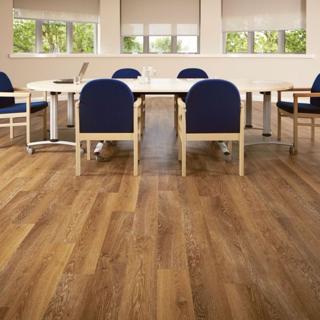 Office space with taupe walls and copper-toned wood floor, with large clock and bank of windows overlooking meeting table and chairs