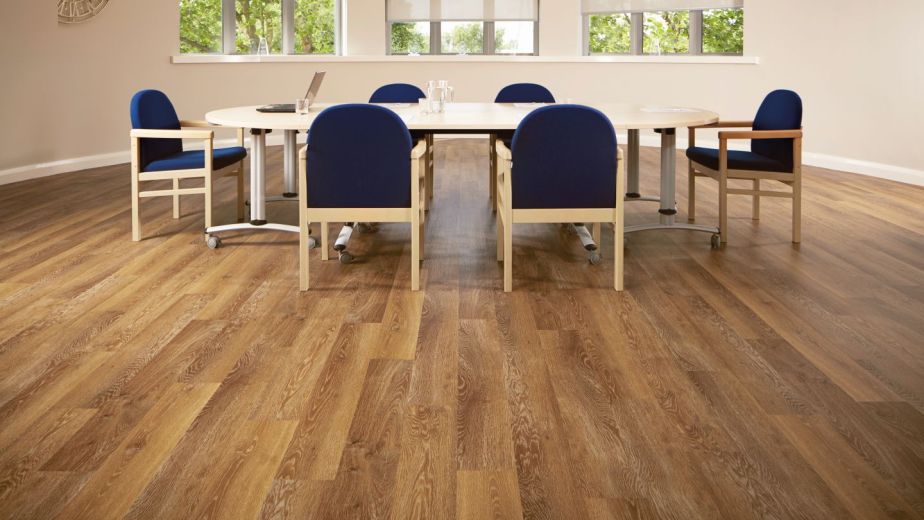 Office space with taupe walls and copper-toned wood floor, with large clock and bank of windows overlooking meeting table and chairs