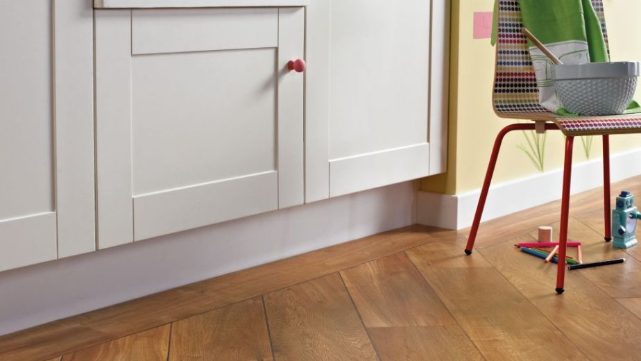 Kitchen space with white cabinetry, farm sink, colorful chair, and natural wide-plank wood floors installed at an angle with decorative design borders