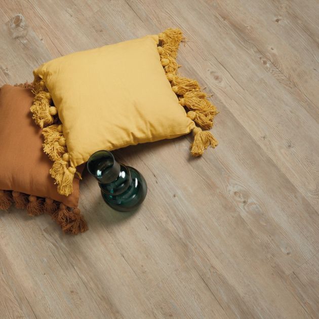 Two decorative pillows and dark glass vase on neutral woodgrain floor
