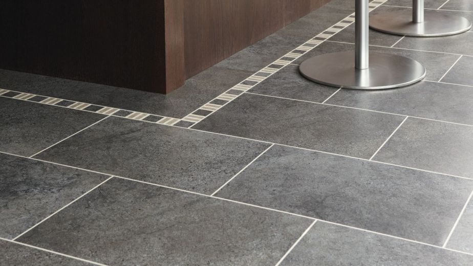 Kitchen island lined with decorative border, gray tile floor, and silver bar stool legs