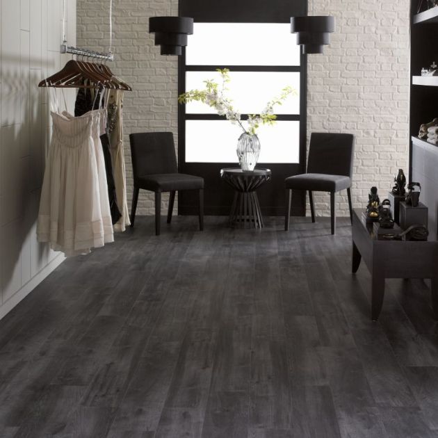Retail space featuring black woodgrain floors, with two chairs and table stationed before frosted window, with dress rack and shoe shelving nearby