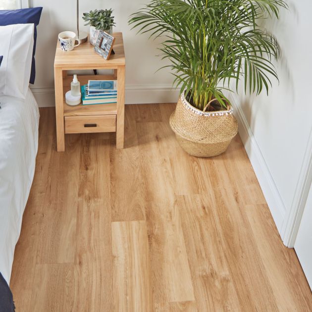 Coastal bedroom with white and blue bedding, wooden nightstand, and potted palm houseplant in room with blond oak LVP floors