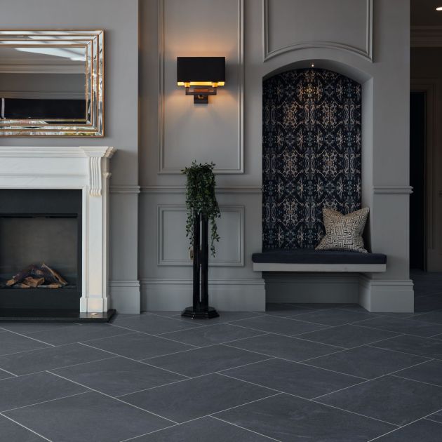 Dark, dramatic living space with white fireplace, gold mirror, sconce, houseplant, and alcove area, with off-white wainscoted walls and rectangular charcoal tiles staggered and grouted
