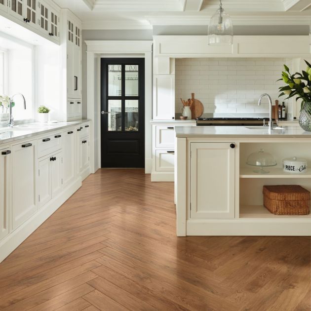 Bright kitchen with white cabinetry, black door, and white island, with silver glass pendant lights, and warm medium brown herringbone woodgrain LVP floor