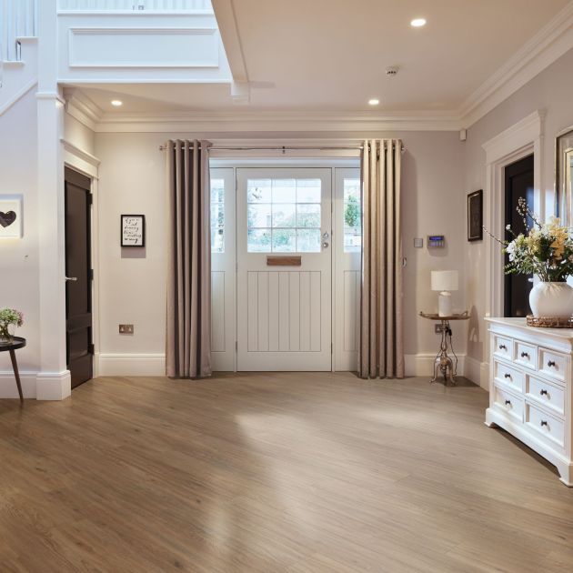 Merino Oak medium brown LVP flooring installed in a diagonal in entryway, with white farmhouse door, curtains, side table, and buffet table