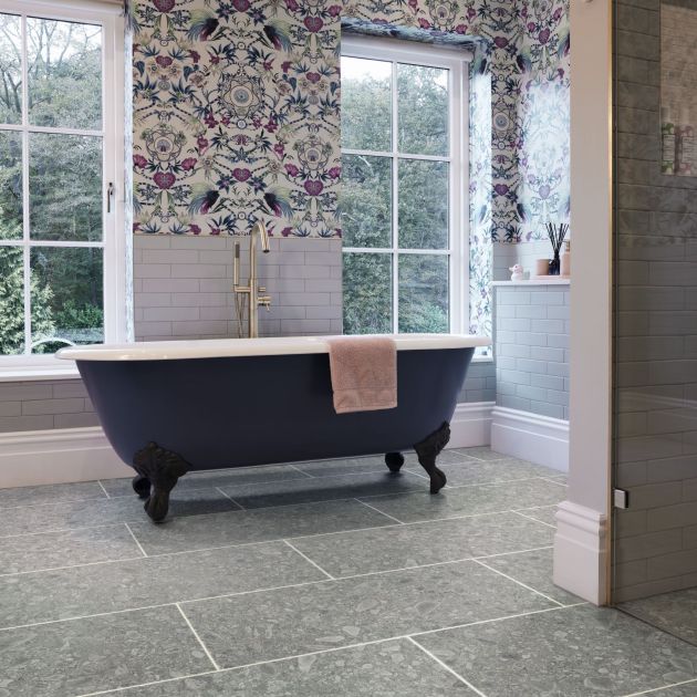 Bathroom scene with clawfoot tub before two large windows, with floral wallpaper and wall tile and gray rectangular terrazzo-look LVT with grout lines