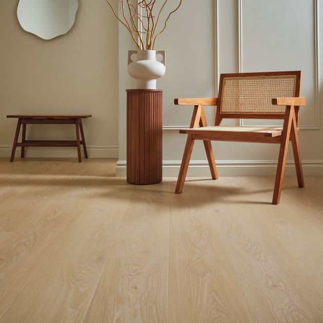 Wooden chair and small wooden cylindrical side table topped with pottery and dried branches, with small wooden bench and mirror in background, in living area with wainscoting and taupe wood-pattern floors
