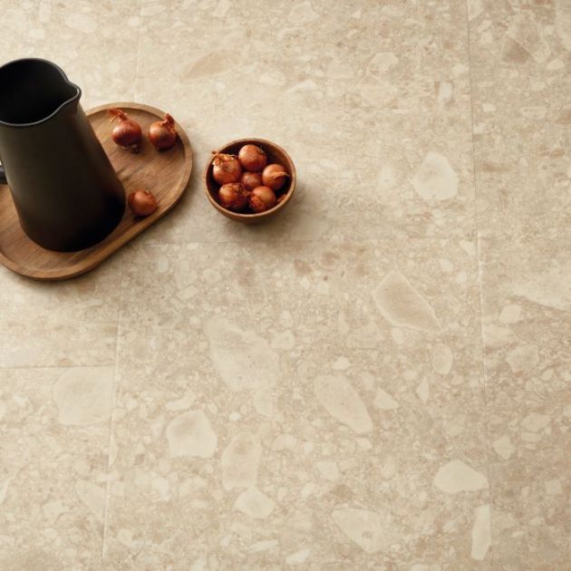 Overhead shot of modern black pitcher atop wooden tray, beside bowl of onions on beige and taupe terrazzo tile