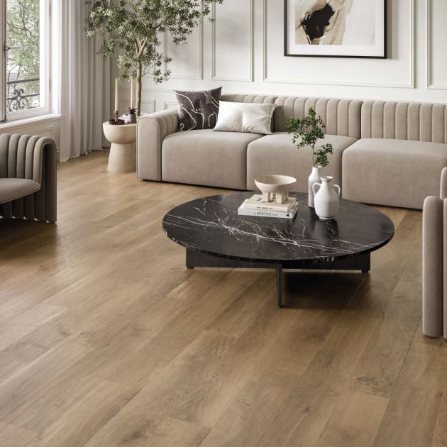 Calm neutral living space with modern couch, armchairs, black marble coffee table topped with pottery, with artwork and large houseplant on muted brown woodgrain floor