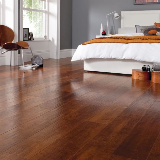 Bedroom with modern artwork hanging behind bed, wooden chair, windows, and wooden bins on reddish brown cherry woodgrain floor with hand-scraped texture