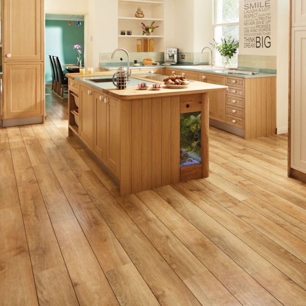 Bright kitchen with warm-toned wood cabinetry, island, and blonde woodgrain floor, with peek of dining area in background