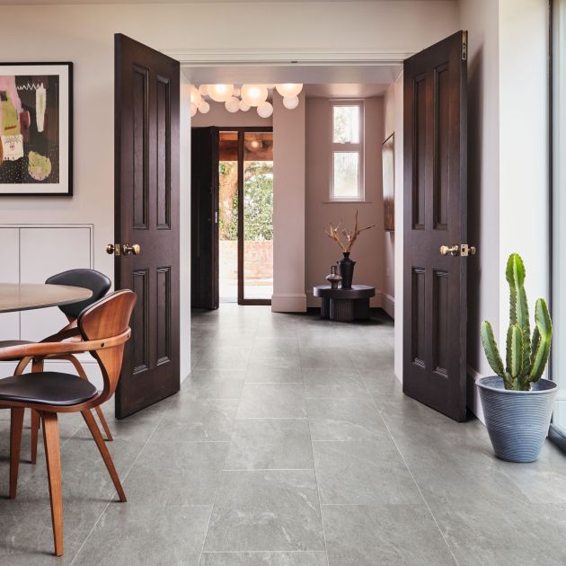 Dining space with artwork, modern chairs, and potted cactus looking beyond wooden doors into entry area with low corner table