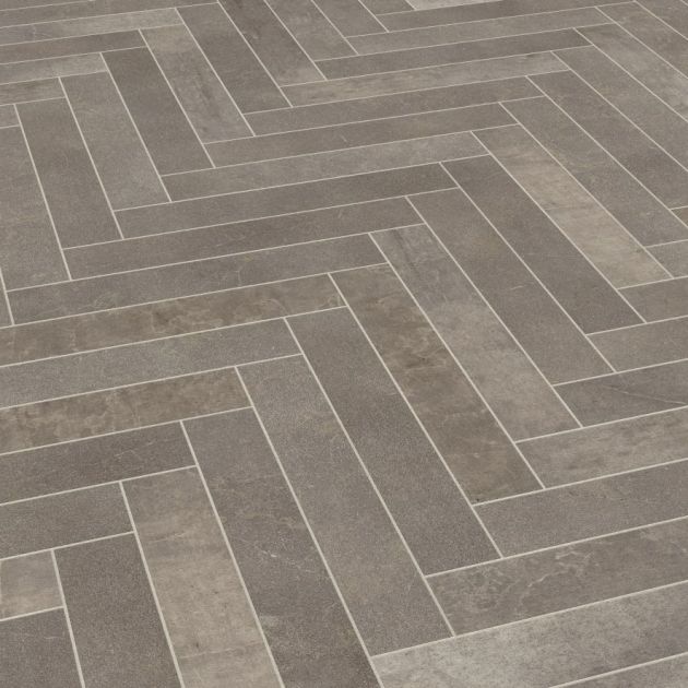Sample of Fumo herringbone LVT, a smokey gray tile with stone texture, shade variation, and grout strips between tiles