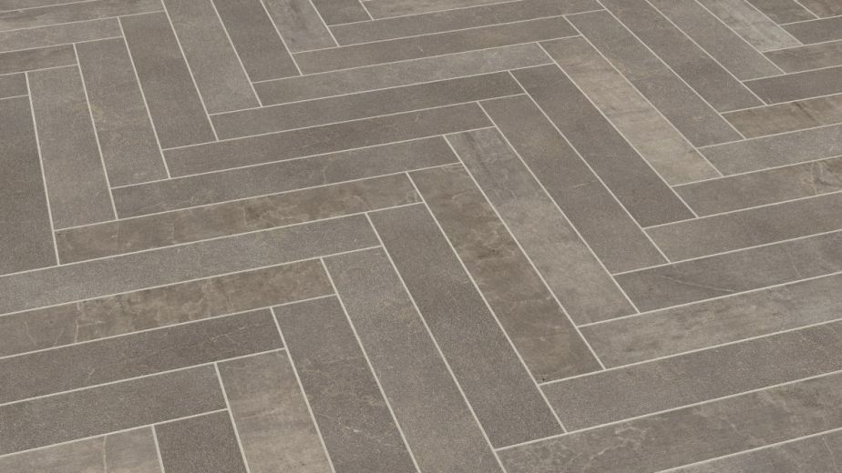 Sample of Fumo herringbone LVT, a smokey gray tile with stone texture, shade variation, and grout strips between tiles