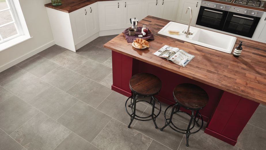 Kitchen space with gray tile floor and maroon island with butcherblock counter and sink, with croissants, coffee, and magazine positioned near two stools