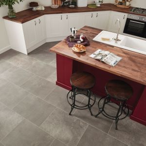 Kitchen space with gray tile floor and maroon island with butcherblock counter and sink, with croissants, coffee, and magazine positioned near two stools