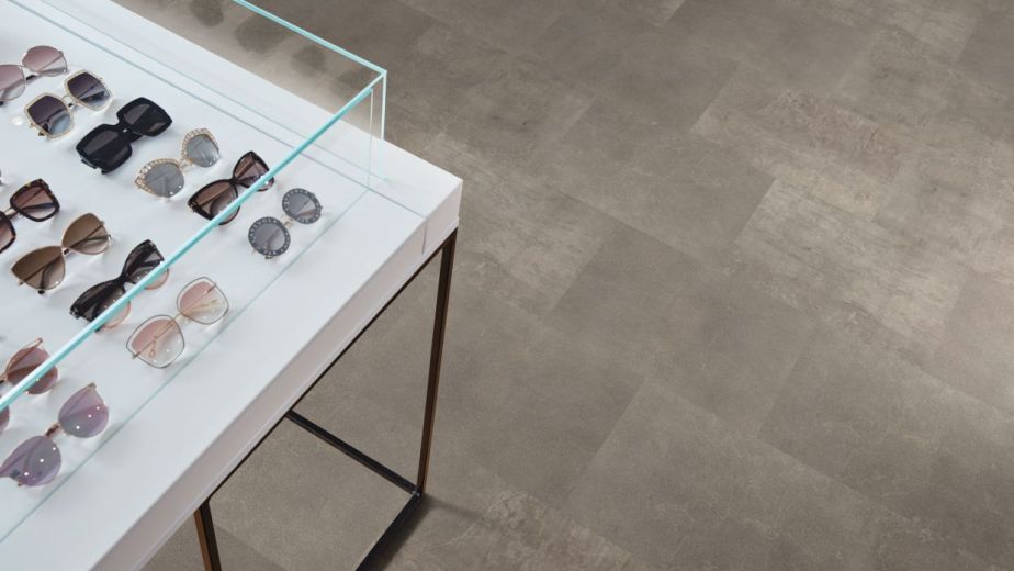 Retail space featuring various sunglasses in display table with rectangular gray tile floor