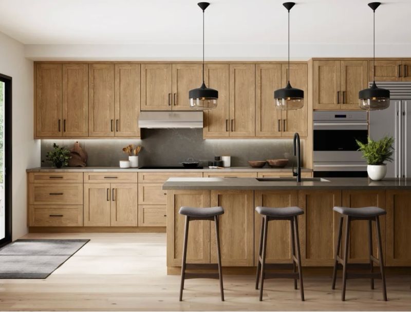 Modern kitchen with medium wood cabinets and island with dark charcoal countertops and backsplash, with industrial black pendants lights, with entry mat over light wooden floors