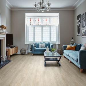 Living space with deer painting hanging over fireplace, with blue couch and loveseat flanking coffee table, TV in corner, and silver chandelier with beige and taupe woodgrain LVP flooring