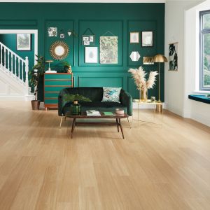Living space with green velvet sofa, green feature wall with wainscoting and artwork, in space with blond oak floors, with peek at white staircase in background