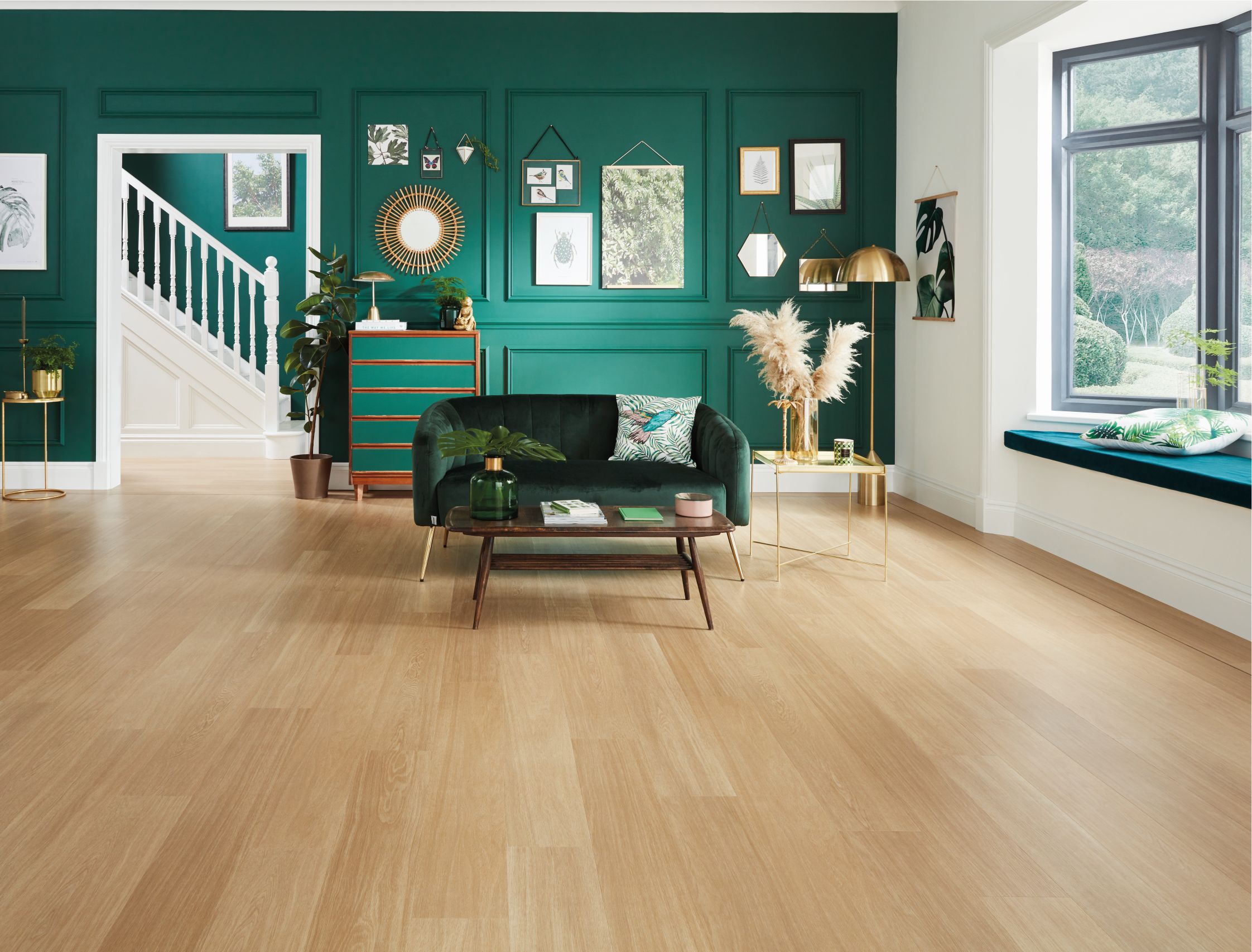 Living space with green velvet sofa, green feature wall with wainscoting and artwork, in space with blond oak floors, with peek at white staircase in background