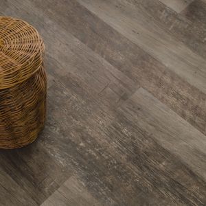 Wicker laundry hamper with towel peeking out on weathered gray-brown plank floor