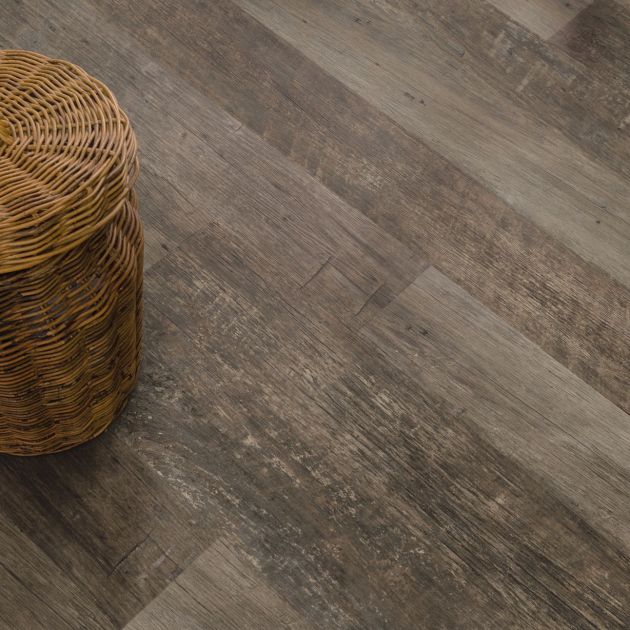 Wicker laundry hamper with towel peeking out on weathered gray-brown plank floor