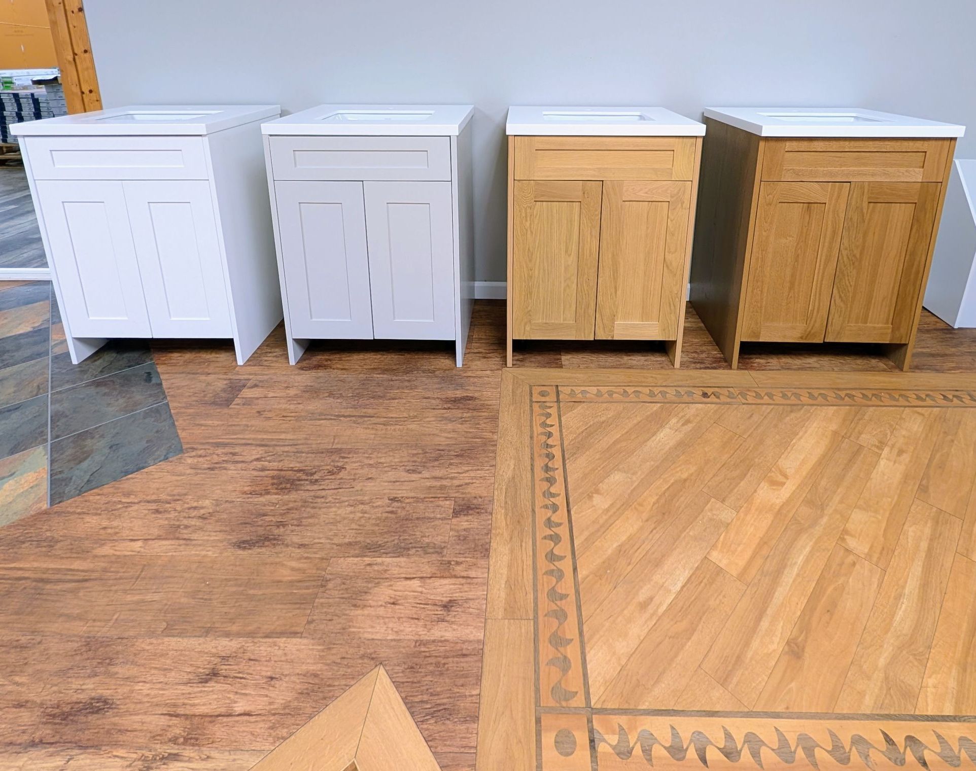 Four bathroom vanity display models with white sinks over floor vignettes