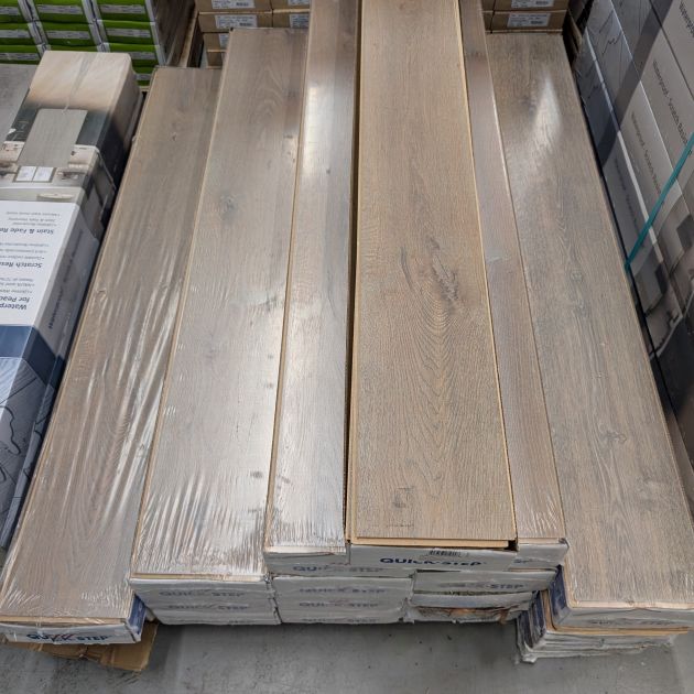 Tannin Oak laminate plank samples atop closed white boxes on pallet, with other boxes visible in background
