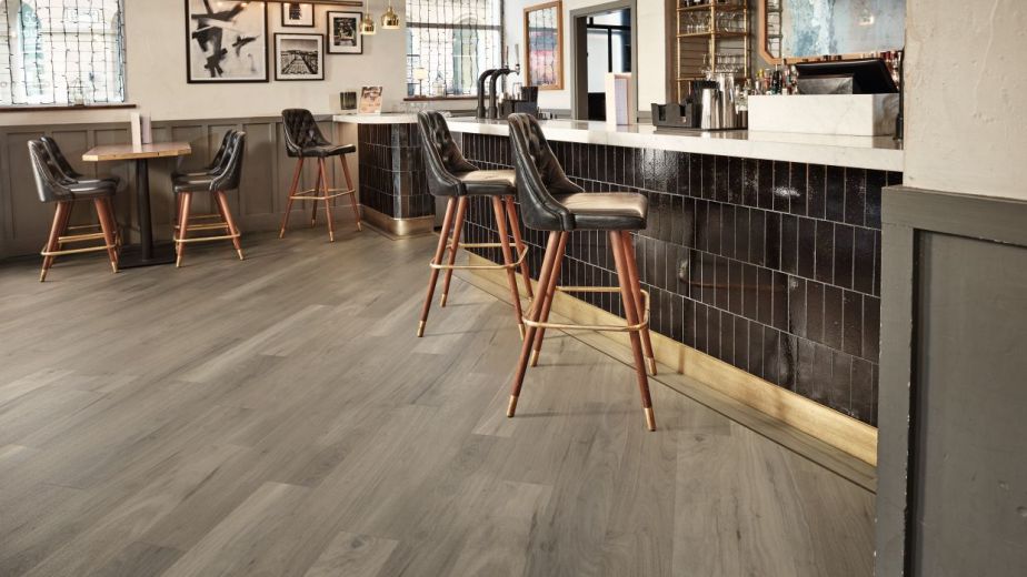 Modern bar space with black tile, weathered gray woodgrain floor installed on a diagonal, and various leather barstools and chairs