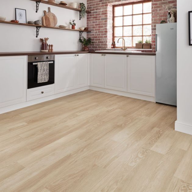 White kitchen with exposed brick wall, large window, and pale brown woodgrain floor