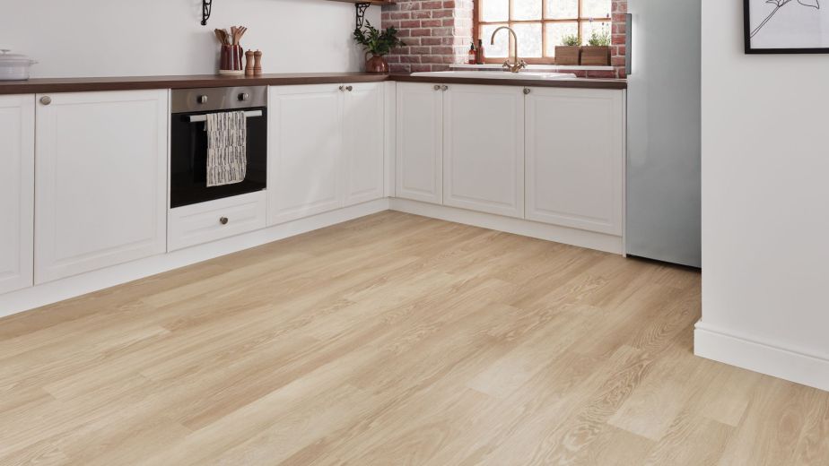 White kitchen with exposed brick wall, large window, and pale brown woodgrain floor