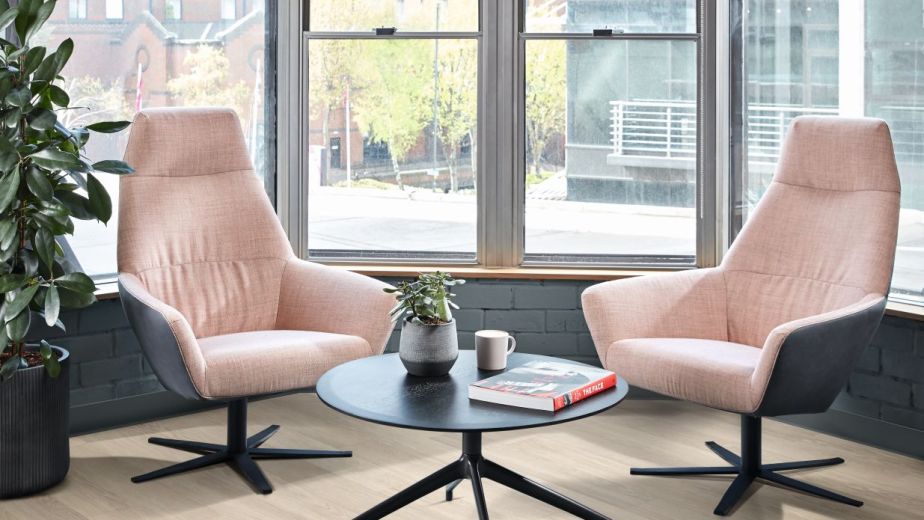Office space featuring two office chairs and central table before large glass windows and houseplant, with industrial buildings visible in background
