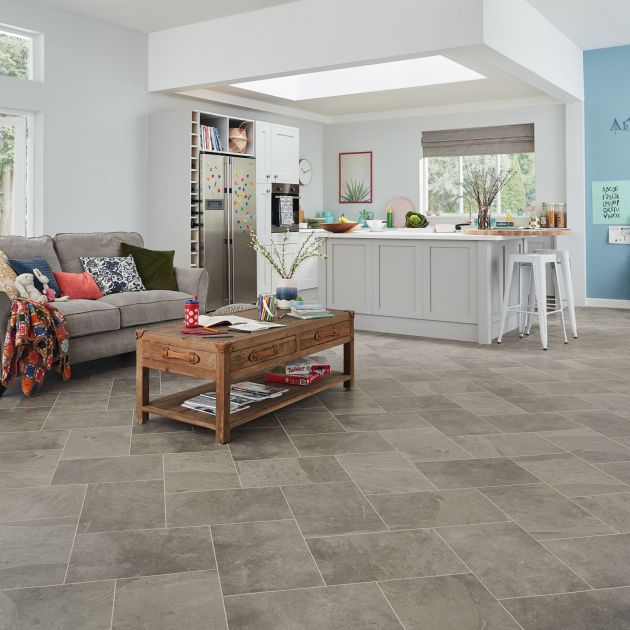 Open-concept living and kitchen area with skylight over island, couch with toys, and children's artwork on wall, with gray LVT floor installed at a diagonal