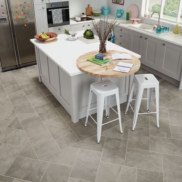 Kitchen with gray cabinetry, island with two metal stools, and refrigerator over grouted gray LVT floor installed to emphasize island