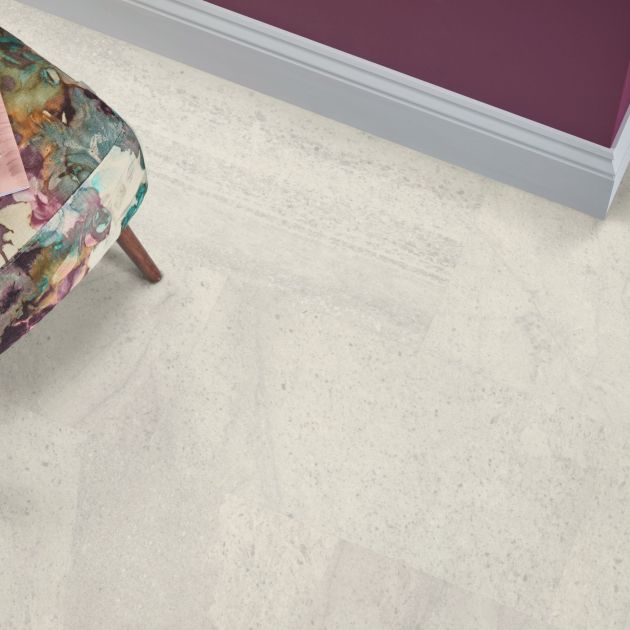 Floral patterned armchair atop pale gray and cream rectangular stone-look LVT floor, with maroon wall