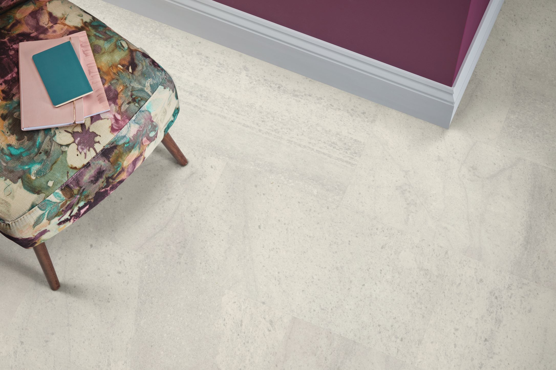 Floral patterned armchair atop pale gray and cream rectangular stone-look LVT floor, with maroon wall