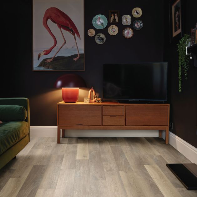 Living space with flamingo artwork above TV console, with couch across from fireplace, in dark room with taupe woodgrain LVP flooring