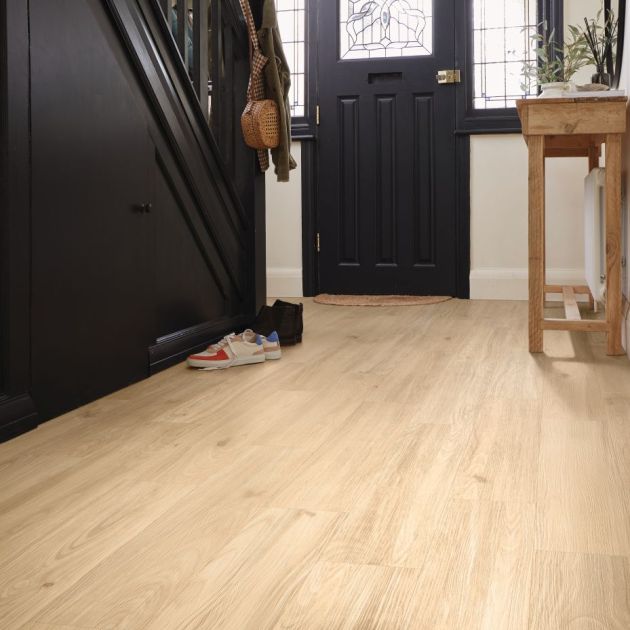 Hallway with black staircase, black front door, and light golden brown woodgrain LVP floor, with entry table and shoes nearby