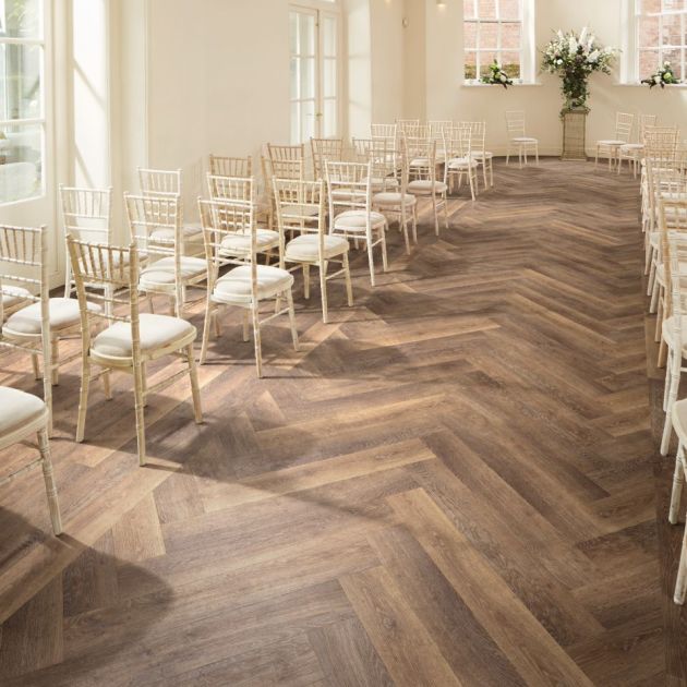 Wedding venue featuring rows of rustic wooden chairs facing alcove, with natural light and chevron-pattern pale brown woodgrain LVP floor