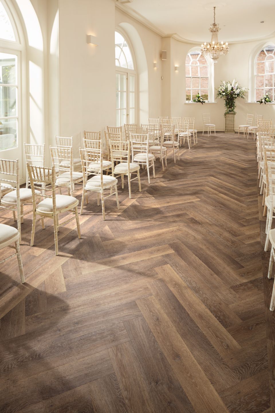 Wedding venue featuring rows of rustic wooden chairs facing alcove, with natural light and chevron-pattern pale brown woodgrain LVP floor