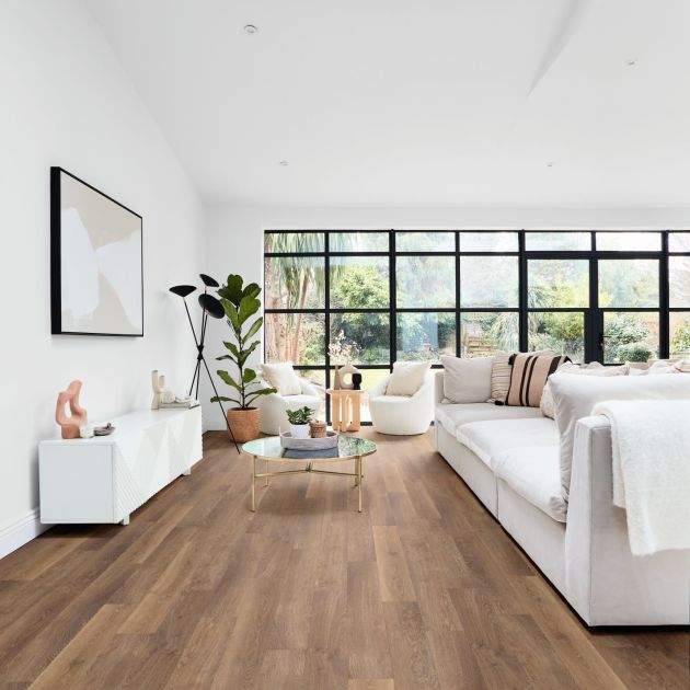 Living space with white couch facing credenza and artwork, with large black framed windows in background and golden brown woodgrain LVP floor