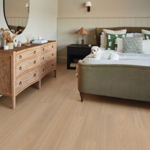 Clean, cozy bedroom with wooden dresser, mirror, and small dog sitting on bed, in room with beadboard walls and clean taupe woodgrain floors