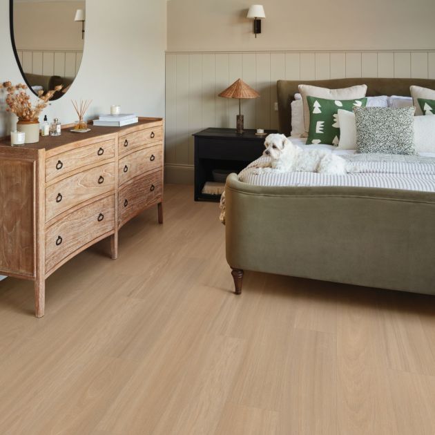 Clean, cozy bedroom with wooden dresser, mirror, and small dog sitting on bed, in room with beadboard walls and clean taupe woodgrain floors